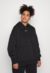 Čierna mikina s kapucňou vyrobená z mäkkej látky, s klokankovou kapsou, káblovou kapucňou a bielym logom Nike na hrudi. Má voľný strih a rebrované manžety.