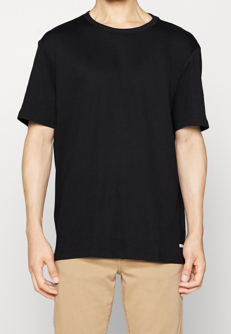 T-shirt nera in cotone con scollo a giro, maniche corte e vestibilità rilassata. Presenta un design semplice senza motivi o accessori visibili.