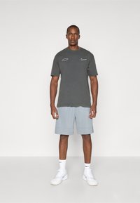 Dark gray cotton t-shirt with white Chevrolet and Nike logos, paired with light gray shorts. Model wears white sneakers and socks.