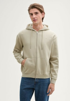 Beige zip-up hoodie with a drawstring hood, two front pockets, and a small logo on the chest. Made of soft, cotton-blend fabric.