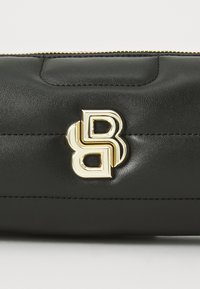 Black leather bag featuring a quilted design, gold-tone logo hardware, and a top zipper closure. Smooth texture with stitched detailing.