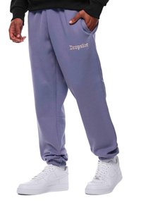 Světle fialové teplákové kalhoty s elastickými manžetami a bočními kapsami, zdobené vyšitým nápisem "Dropsize" v kontrastní barvě, spárované s bílými teniskami.
