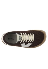 Zapatilla de ante marrón oscuro con detalles blancos, que presenta una puntera redondeada, suela de goma beige y cordones blancos. Logo visible en la plantilla.