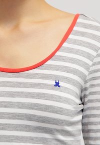 T-shirt rayé gris et blanc avec un col rond et une bordure couleur corail, comportant un petit logo bleu sur la poitrine. Matière en coton doux.