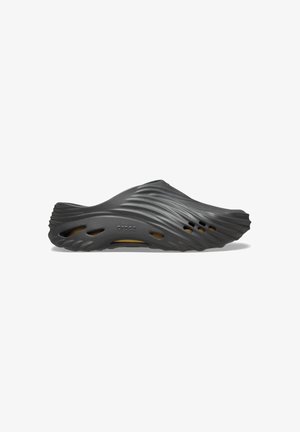 Sabot en caoutchouc noir avec un design ondulé, présentant des trous de ventilation et une surface douce et texturée. Léger avec une forme contour.