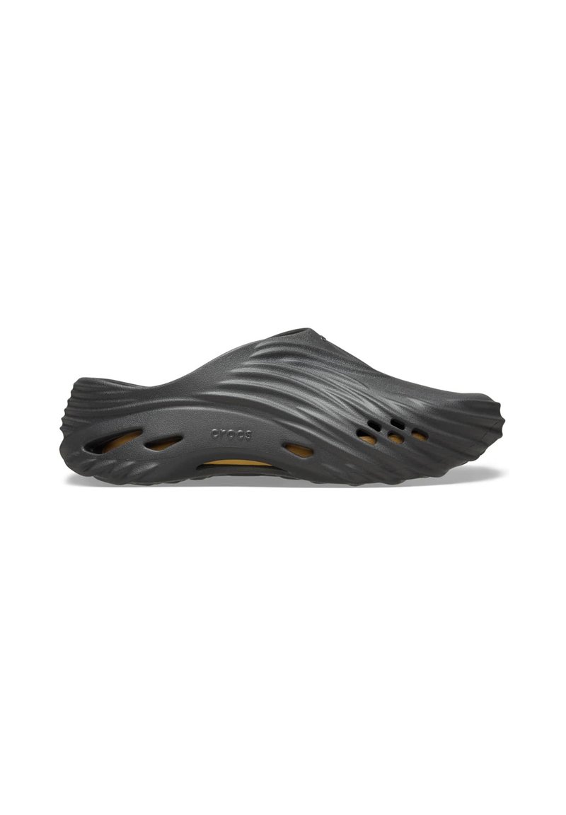 Sabot en caoutchouc noir avec un design ondulé, présentant des trous de ventilation et une surface douce et texturée. Léger avec une forme contour.