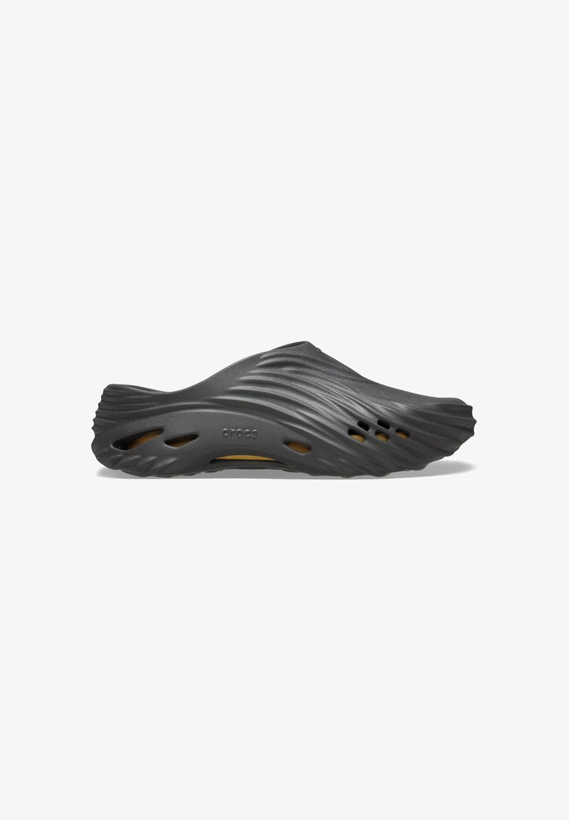 Sabot en caoutchouc noir avec un design ondulé, présentant des trous de ventilation et une surface douce et texturée. Léger avec une forme contour.