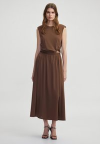 Bruine twee-delige outfit bestaande uit een mouwloze, aansluitende top met een knoopdetail en een hoge, vloeiende maxi-jurk. Glad textuur.