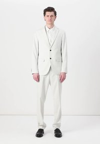 Hvidt pinstriped jakkesæt med en enkeltknap blazer og matchende bukser. Glat stof, subtil tekstur, parret med sorte sko.