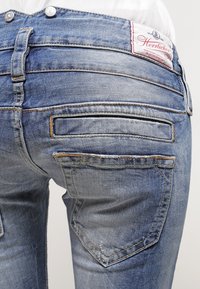 Blå denimjeans med en urtvättad finish, med två bakfickor och synliga sömdetaljer. Midjebandet har en etikett med varumärket.