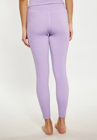 Paarse leggings met een zachte textuur, een aansluitend ontwerp en een brede tailleband, weergegeven vanuit een achteraanzicht met blote voeten.