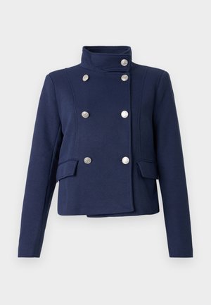 Navy blue double-breasted jacket with a funnel neck, silver round buttons, two front pockets, and structured shoulders. Soft fabric texture.