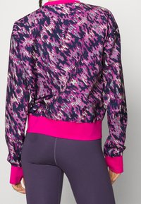 Lila und rosa gemusterter Pullover mit einem rosa gerippten Saum und Bündchen, der ein strukturiertes abstraktes Design auf einem dunklen Hintergrund zeigt.