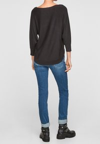 Czarny top z długim rękawem i okrągłym dekoltem, w połączeniu z niebieskimi wąskimi dżinsami, podwiniętymi na kostkach, oraz czarnymi botkami na kostkę z ćwiekami.