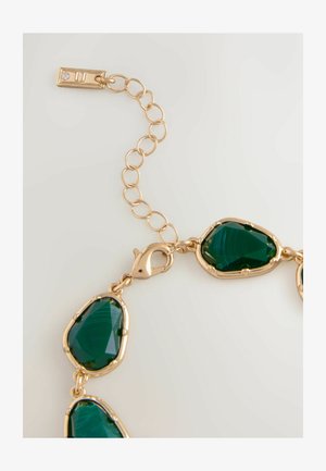 Złocony naszyjnik z nieregularnymi zielonymi kamieniami szlachetnymi o polerowanej powierzchni i połączonym łańcuszku. Posiada zapięcie oraz regulowaną sekcję łańcuszka.