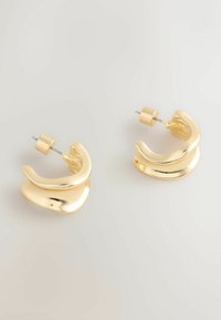 Zelta krāsas metāla riņķa auskari ar gludu, spīdīgu virsmu. Ir izliekta forma un aizdare ar spiedpogu drošai valkāšanai.