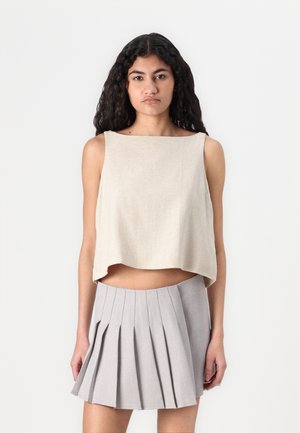 Beige zkrácený top s obdélníkovým výstřihem, spárovaný se světle šedou mini sukní s plisováním, která má vertikální záhyby a hladkou texturu.