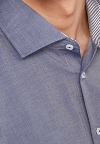 Blårandig skjorta med klassisk krage, knäppningar och en texturerad tyg. Märkbar kontrasterande vit inre kragmönster.