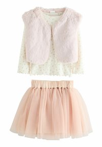 Gilet en fausse fourrure rose clair sur un top à manches longues blanc avec des motifs floraux ; associé à une jupe pale rose en tulle, de style superposé.