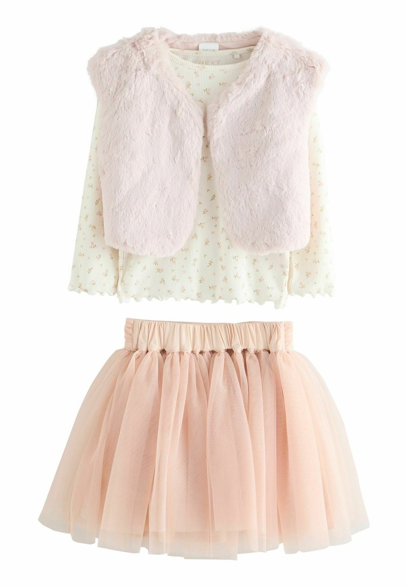 Gilet en fausse fourrure rose clair sur un top à manches longues blanc avec des motifs floraux ; associé à une jupe pale rose en tulle, de style superposé.