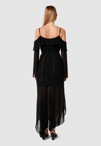 Čierne šaty s priesvitnými dlhými rukávmi, off-shoulder výstrihom, volánovými detailmi a zúženým pásom so šnúrkou. Voľný sukňový strih a asymetrický lem.