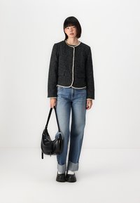 Giacca in tweed nera con scollo rotondo, bordata in crema, abbinata a jeans azzurri chiari e una borsa a spalla nera. L'outfit presenta una vestibilità comoda.