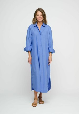 Abito camicia azzurro chiaro con design dritto, maniche lunghe, fessure laterali e tasca sul petto. Tessuto in cotone morbido e vestibilità rilassata.
