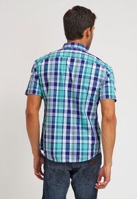 Kortärmad skjorta med rutor i turkos, marinblått och vitt. Har en spridd krage och knäppningsdesign. Tyget verkar vara slätt och lätt.