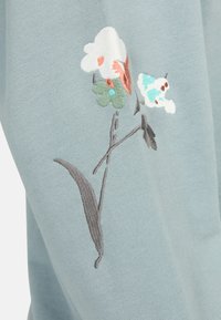 Light blue sweater featuring detailed floral embroidery in white, orange, and green on the sleeve, with a soft, textured fabric.
