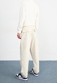Krämfärgade bomullscargobyxor med två bakfickor, avslappnad passform och rak benform, matchade med vita och marinblå sneakers.