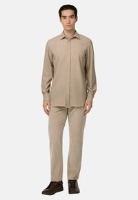 Beige overhemd met lange mouwen en knoopsluiting, gecombineerd met bijpassende beige broek met textuurpatroon en donkerbruine sneakers. Eenvoudige, nauwsluitende pasvorm.