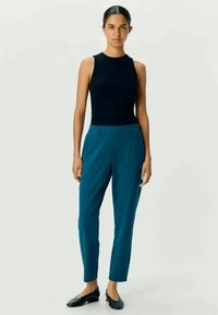 Teal broek met een tailored fit en voorplooien, gecombineerd met een mouwloos zwart topje, afgemaakt met zwarte flats. Glad stof en eenvoudig ontwerp.