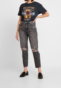 Svart grafisk t-shirt med Led Zeppelin-design; höga grå jeans med slitna detaljer; svarta loafers. Enkelt, avslappnat outfit.