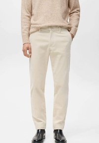 Pantalones de pana beige claro con un diseño de pierna recta, que presentan sutiles nervaduras verticales y un cierre de botón. Combinados con botas de cuero negras.