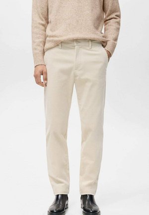 Pantalones de pana beige claro con un diseño de pierna recta, que presentan sutiles nervaduras verticales y un cierre de botón. Combinados con botas de cuero negras.