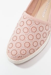 Chaussure rose à enfiler avec des découpes circulaires et des strass argentés incrustés, dotée d'une semelle tressée blanche.