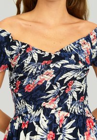 Robe florale décolletée avec une base marine, des feuilles roses et blanches, un corsage smocké et des manches courtes. Tissu léger.