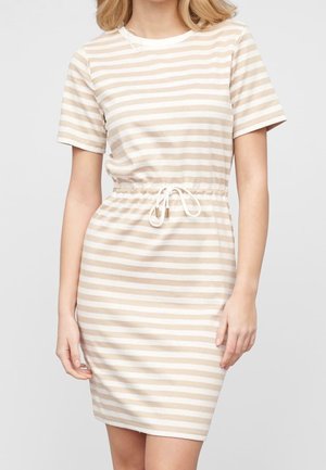 Frau trägt ein kurzärmeliges Kleid mit beigen und weißen horizontalen Streifen und einem Taillenzug, steht vor einem schlichten Hintergrund.