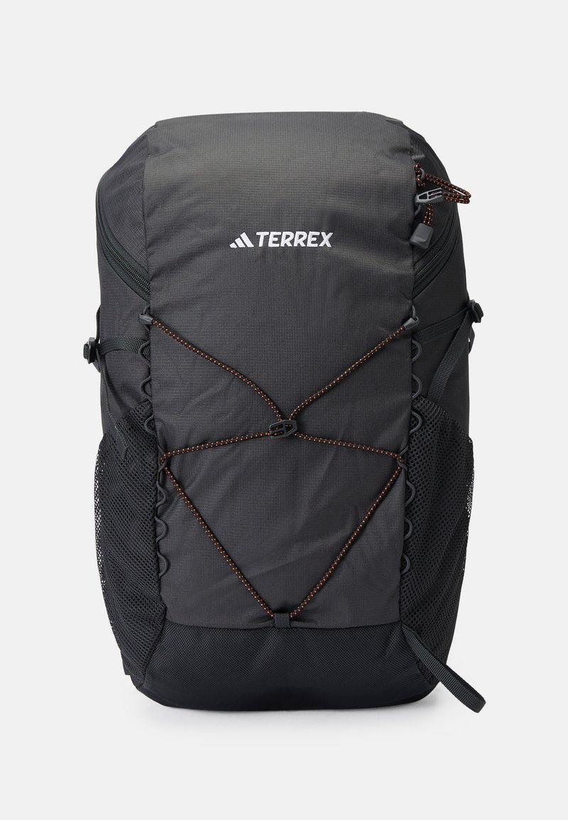 Mochila Terrex negra con una superficie texturizada, bolsillos laterales de malla y un acento de cordón elástico naranja. Presenta correas ajustables y un asa en la parte superior.