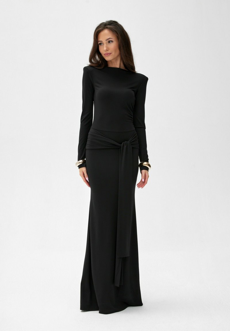 Czarna sukienka z długim rękawem, dopasowanym gorsetem, drapowanym węzłem w talii oraz złotymi akcentami przy mankietach. Gładki, elastyczny materiał. Sukienka sięgająca do ziemi.