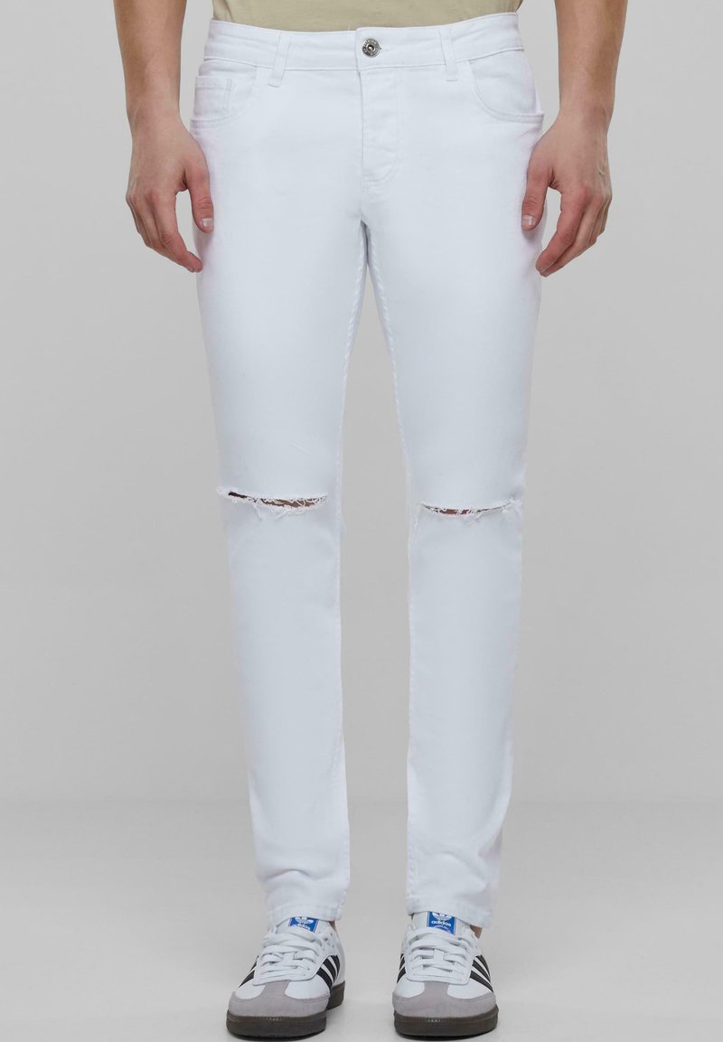 Blugi din denim alb, cu găuri distruse la genunchi, cu un design ajustat și stil standard cu cinci buzunare, asortați cu adidași albi.