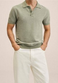 Polo vert en maille avec col et poignets côtelés, coupe ajustée, patte à deux boutons, associé à un pantalon de couleur crème.