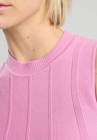 Hihaton vaaleanpunainen neulepaita, jossa on ribbireunat ja pystysuorat paneelit. Sujuva tekstuuri ja vartalonmyötäinen muotoilu, joka korostaa korkeaa kaula-aukkoa.