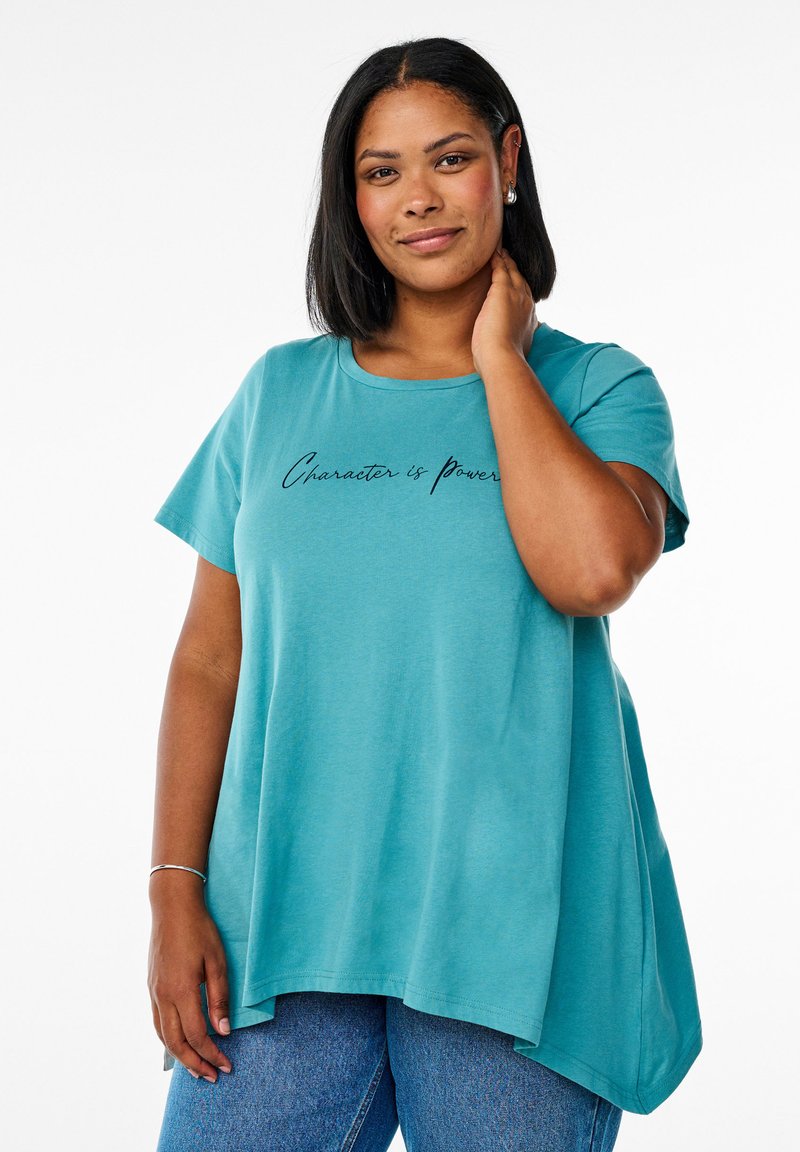 Teal kortærmet t-shirt med buet kant og teksten "Karakter er Magt" i sort kursiv skrifttype. Fremstillet af blødt materiale med en afslappet pasform.