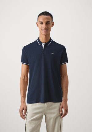 Polo de color navy con un diseño clásico, que presenta un cierre de dos botones, cuello y acentos en las mangas en blanco, y un pequeño logo en el pecho.