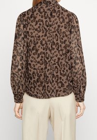 Blouse à imprimé léopard marron à manches longues, avec un col haut et une coupe ample, fabriquée en tissu léger et texturé.