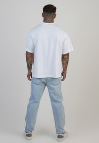 Camiseta blanca de manga corta con un corte holgado, combinada con jeans de color azul claro. Presenta un cuello redondo y un diseño liso sin patrones visibles.