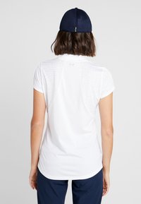 Vit kortärmad sporttröja med en texturerad bakpanel, rund halsringning och curvead nederkant, kombinerad med en marinblå meshkeps.