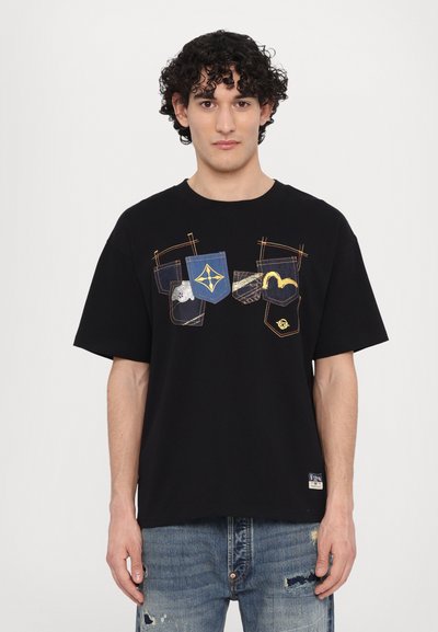 T-shirt noir à manches courtes avec des graphismes de poche en bleu et détails métalliques. Fabriqué en coton doux, coupe décontractée, col rond.