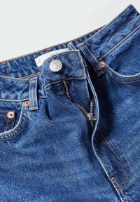 Blauwe denim jeans met een ritssluiting, metalen knoopsluiting en koperen accenten. Zichtbare stikseldetails langs de tailleband en zakken.
